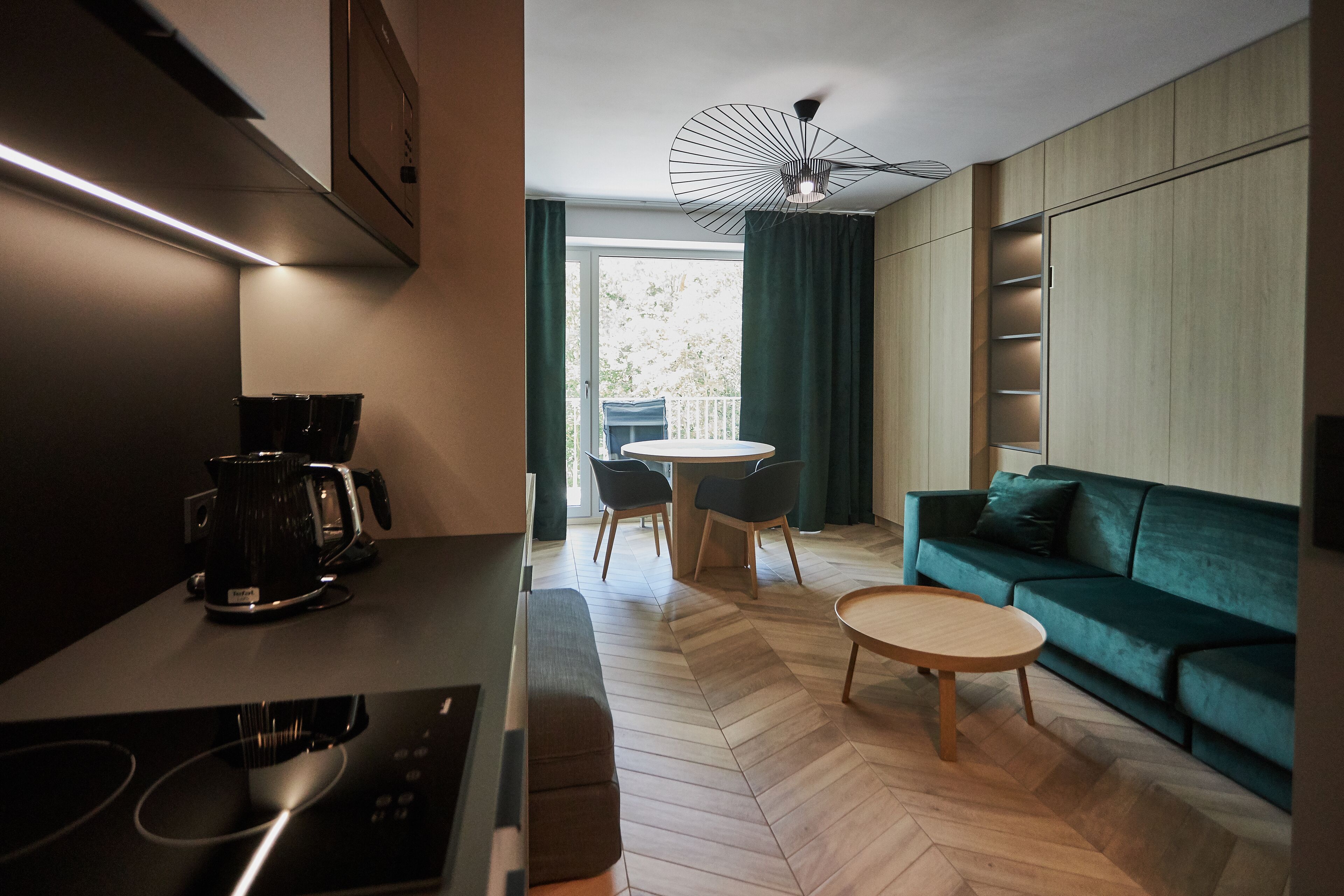 A modern kitchen with a coffee maker, a dining table with chairs, and a green sofa in a living area.