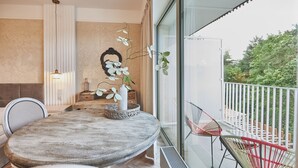 Un coin repas avec une table ronde, des chaises et un vase orné d’orchidées. Il y a également un balcon avec une balustrade et des chaises.