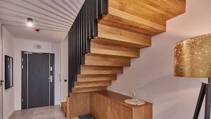 Un escalier moderne avec des marches en bois et une rampe noire, menant à un palier où se trouvent un bureau en bois et une lampe.