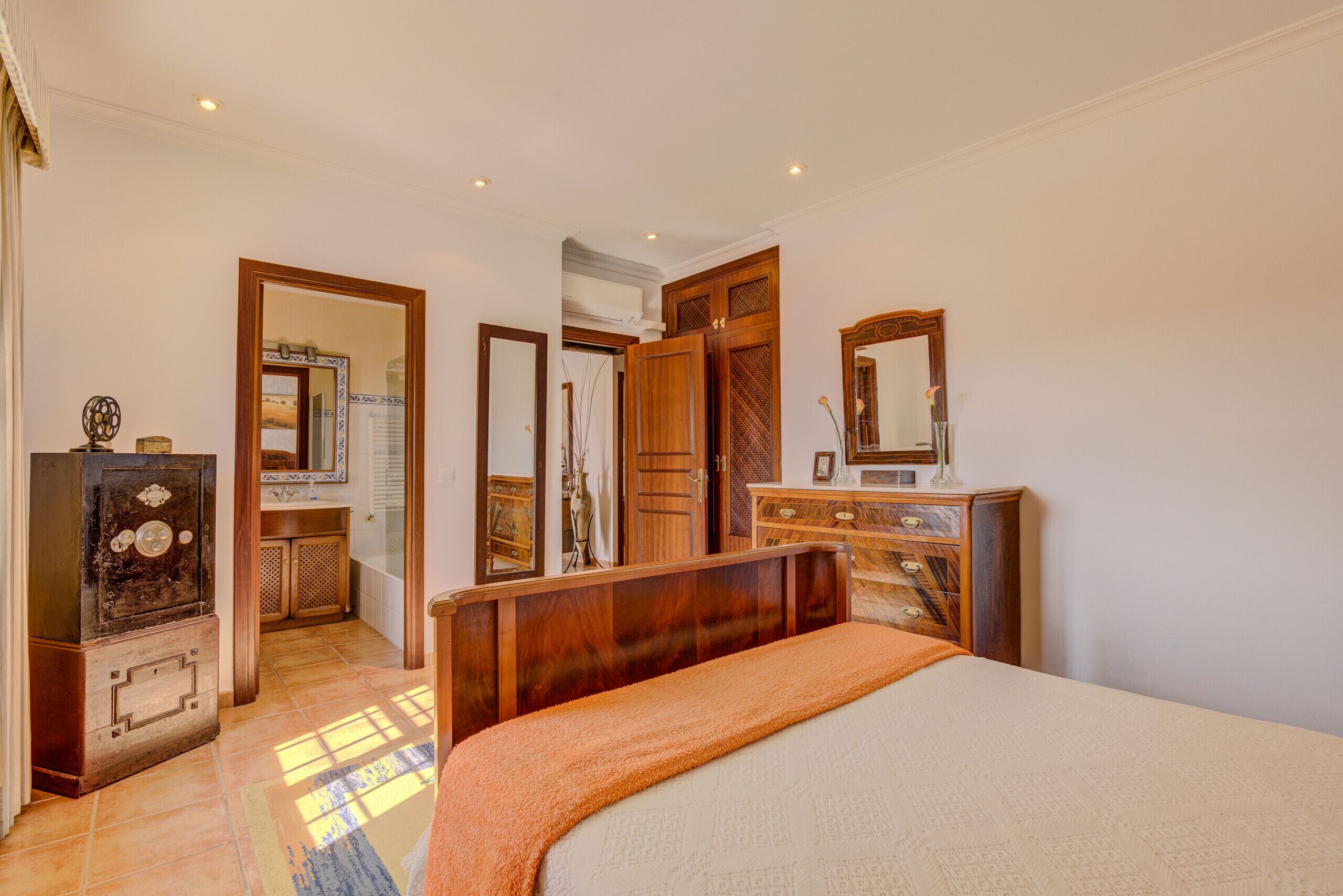 Een slaapkamer met een bed, een houten dressoir en een spiegel.