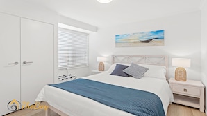 Une chambre à coucher comprenant un lit, des tables de chevet, une fenêtre avec des stores, un tableau au mur et une armoire.