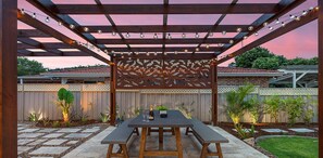 An outdoor patio with a pergola, string lights, and a table set for two.