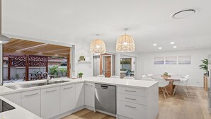 Une cuisine moderne avec des meubles blancs, un lave-vaisselle et des luminaires suspendus.