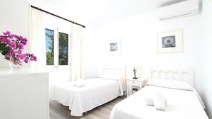 A hotel room with two beds, a desk, a chair, a window with curtains, and a vase of flowers. - Finca Sant Jordi, private pool, quiet location with a view, A/C, Wi-Fi (IB)