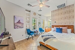 A bedroom with a bed, two blue chairs, a desk, and a large window.