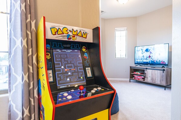 A Pac-Man arcade machine in a room with a television and a wooden cabinet.