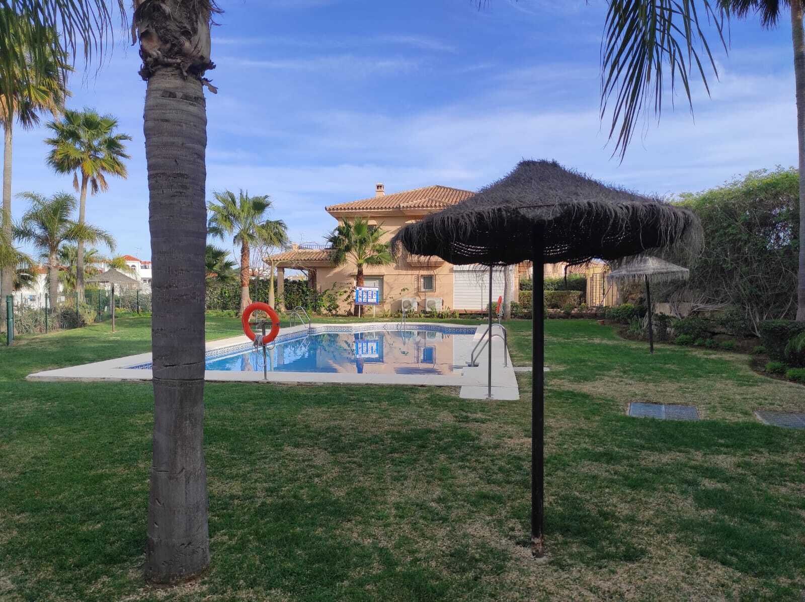 A pool area with a lifeguard stand, palm trees, and a building with a tiled roof in the background.