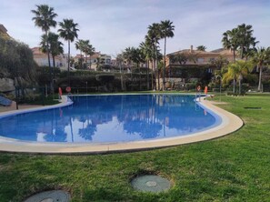 A swimming pool surrounded by grass and palm trees, with a stone wall and buildings in the background. - RIVIERA VILLA WITH PRIVATE POOL (Mijas Costa)
