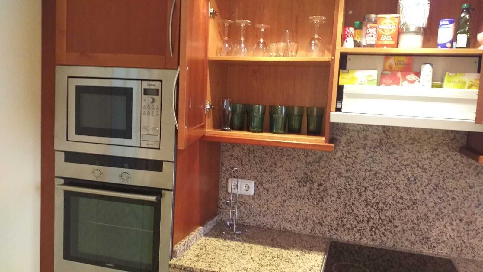 Una cocina equipada con microondas, horno y una alacena con cristalería.