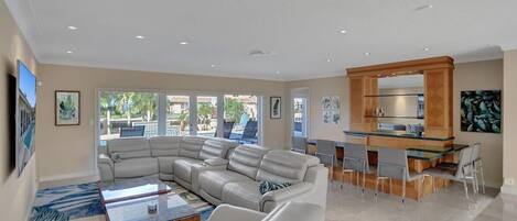 A spacious living area with a large L-shaped sofa, a coffee table, and a dining area with a glass-top table and chairs.