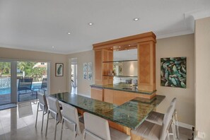 A modern kitchen with a glass island, white chairs, and a view of a swimming pool. - Palms by the Sea Villa 🌊 Waterfront | Heated Pool | Near Beach 🏖️ (Fort Lauderdale)