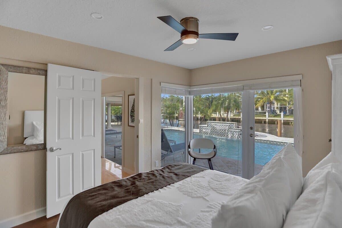 Ein Schlafzimmer mit einem Bett, einem Deckenventilator, einer Tür und Blick auf einen Swimmingpool.