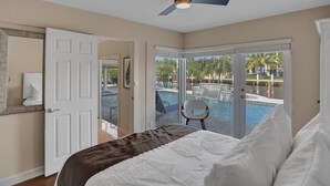 Ein Schlafzimmer mit einem Bett, einem Deckenventilator, einer Tür und Blick auf einen Swimmingpool.
