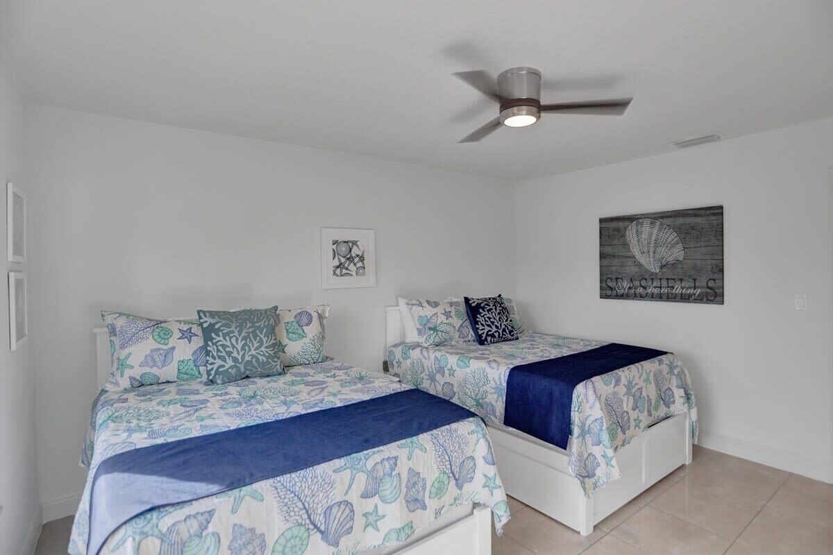 A bedroom with two beds, a ceiling fan, and artwork on the walls.