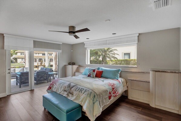 A bedroom with a bed, a bench, a ceiling fan, a window, and an open door leading to a balcony.