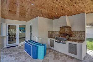 An outdoor kitchen area with a grill, a countertop, and a ceiling with wooden beams.