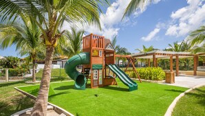 A playground with a slide and climbing structure, surrounded by palm trees and a well-maintained lawn. - Luxury at Pristine Bay Villa 1106 (Roatan)