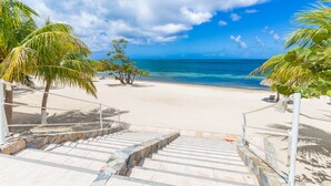 A beach with clear blue water, palm trees, and a staircase leading down to the shore. - Luxury at Pristine Bay Villa 1106 (Roatan)