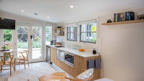A modern kitchen with a dining area, wooden cabinets, and a window overlooking a garden.