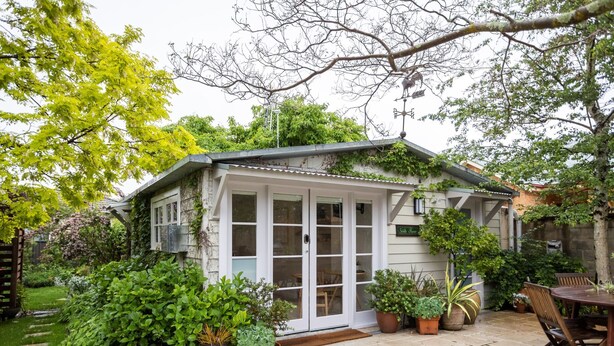 A house with a covered patio, potted plants, and a wooden table.