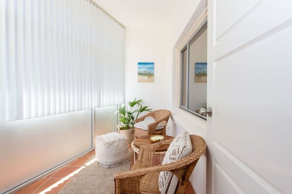 A balcony with wicker furniture, a potted plant, and a painting on the wall.