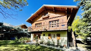 Un chalé de madera con techo inclinado, balcón y jardín con plantas en macetas.