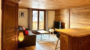 Ein gemütliches Zimmer mit Holzbalkendecke, einer Couch, einem Fernseher und einem kleinen Esstisch.