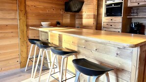 Ein Holzinnenraum mit Küchenbereich, der eine Holzausziehtheke, Barhocker, einen eingebauten Backofen und eine Kaffeemaschine zeigt.