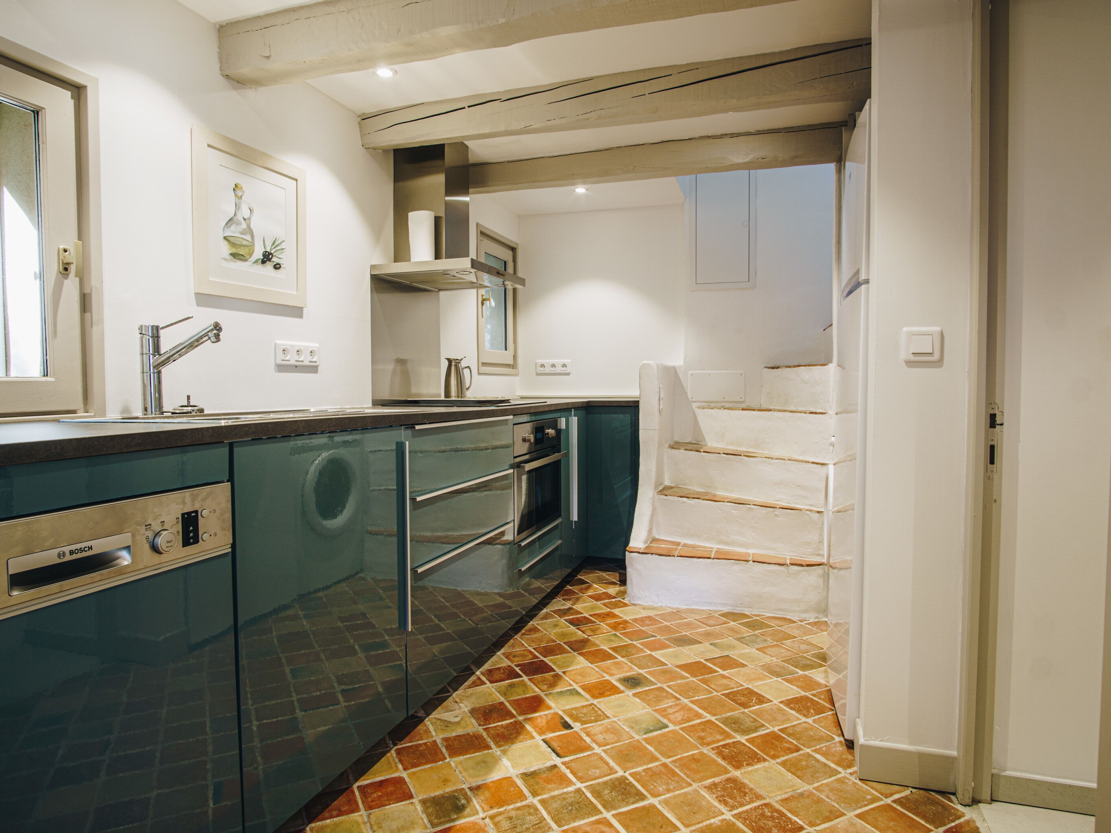 A kitchen with a Bosch dishwasher, a sink, and a staircase leading to another room.