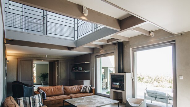 Amplia sala de estar con techo alto, chimenea y balcón con mobiliario exterior.