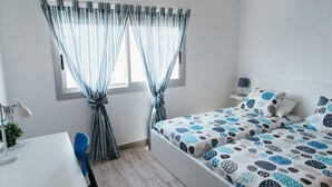 Ein Schlafzimmer mit zwei Betten, einem Schreibtisch, einem Stuhl und einem Fenster mit Vorhängen.