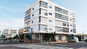 Ein mehrstöckiges Gebäude mit flacher Fassade, großen Fenstern und einem Eingangsbereich im Erdgeschoss.