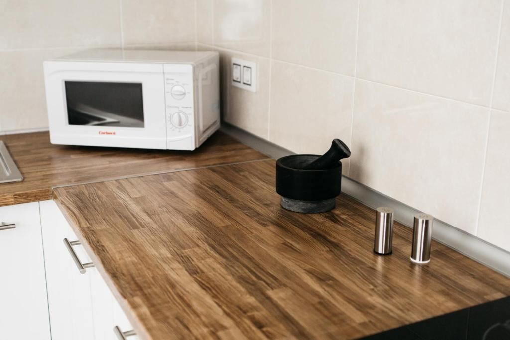 A kitchen with a microwave, a black appliance on the counter, and two metallic containers.