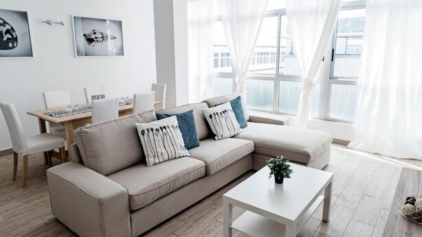 Ein modernes Wohnzimmer mit einem beigefarbenen Sofa, einem weißen Couchtisch und einem Essbereich mit einem Holztisch und Stühlen.