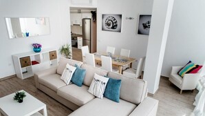 Ein modernes Wohnzimmer mit einem beigefarbenen Sofa, einem weißen Couchtisch und einem Essbereich mit Holztisch und Stühlen.