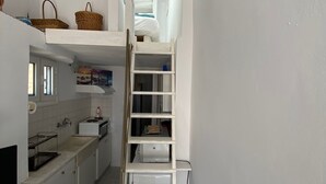 A compact kitchen with a white countertop, a built-in oven, and a white ladder leading to a lofted sleeping area. - S&K Traditional Cycladic House Serifos (Serifos)