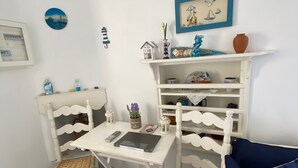 A white room with a white table, two white chairs, a blue cushion, and a shelf with various decorative items. - S&K Traditional Cycladic House Serifos (Serifos)