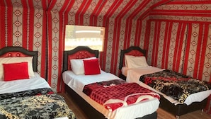 Una habitación con tres camas, cada una con un edredón de diferente estampado. Las paredes tienen papel tapiz rojo y blanco a rayas.