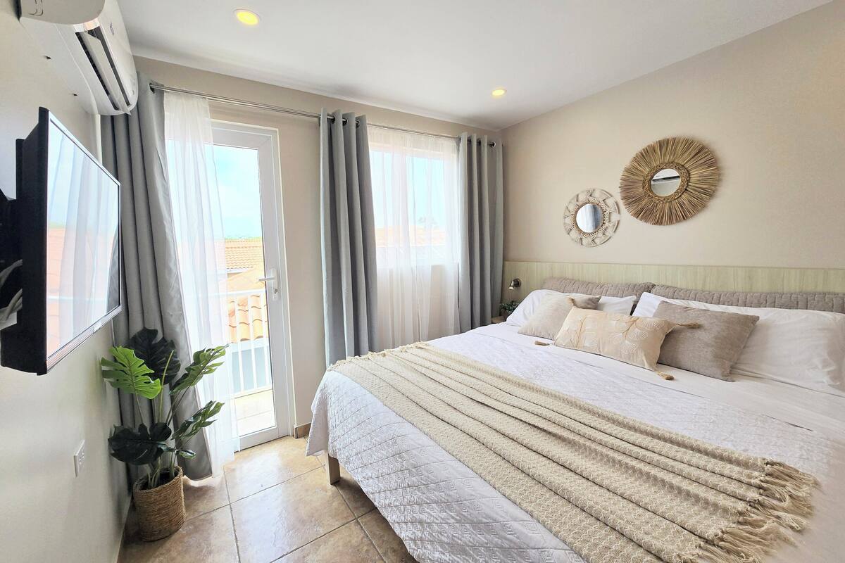 A bedroom with a bed, curtains, a wall-mounted TV, and a potted plant.