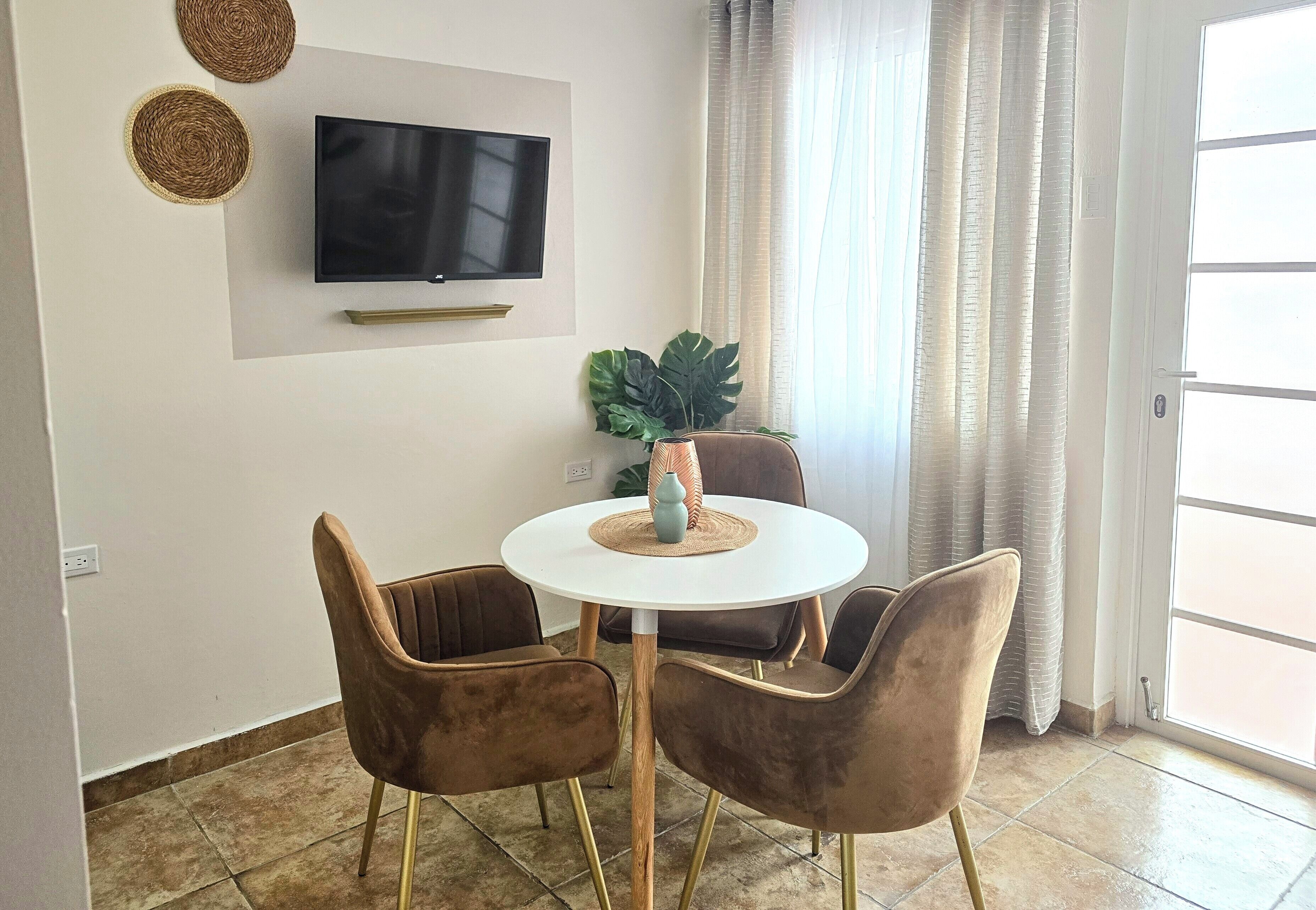 Un coin repas comprenant une table ronde, quatre chaises, un téléviseur fixé au mur et une grande plante.