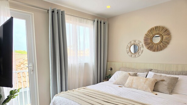 A bedroom with a large bed, a TV, and a view of the outside. - Rooi Santo Residence (Noord)