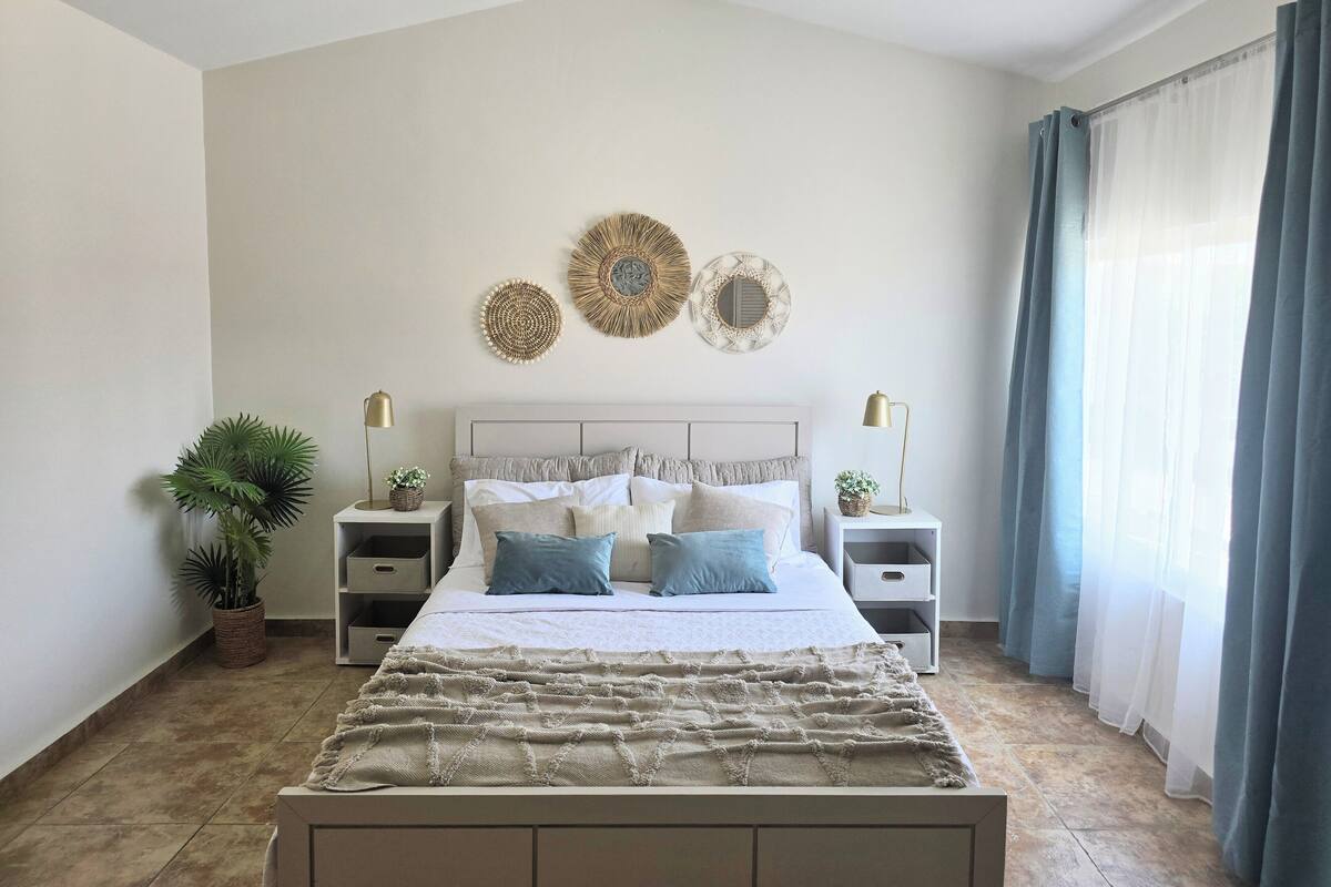 A bedroom with a bed, two bedside tables, a potted plant, and decorative wall art.