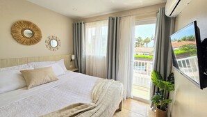 A hotel room with a bed, a TV, a wall-mounted air conditioner, and a view of the outside balcony. - Rooi Santo Residence (Noord)