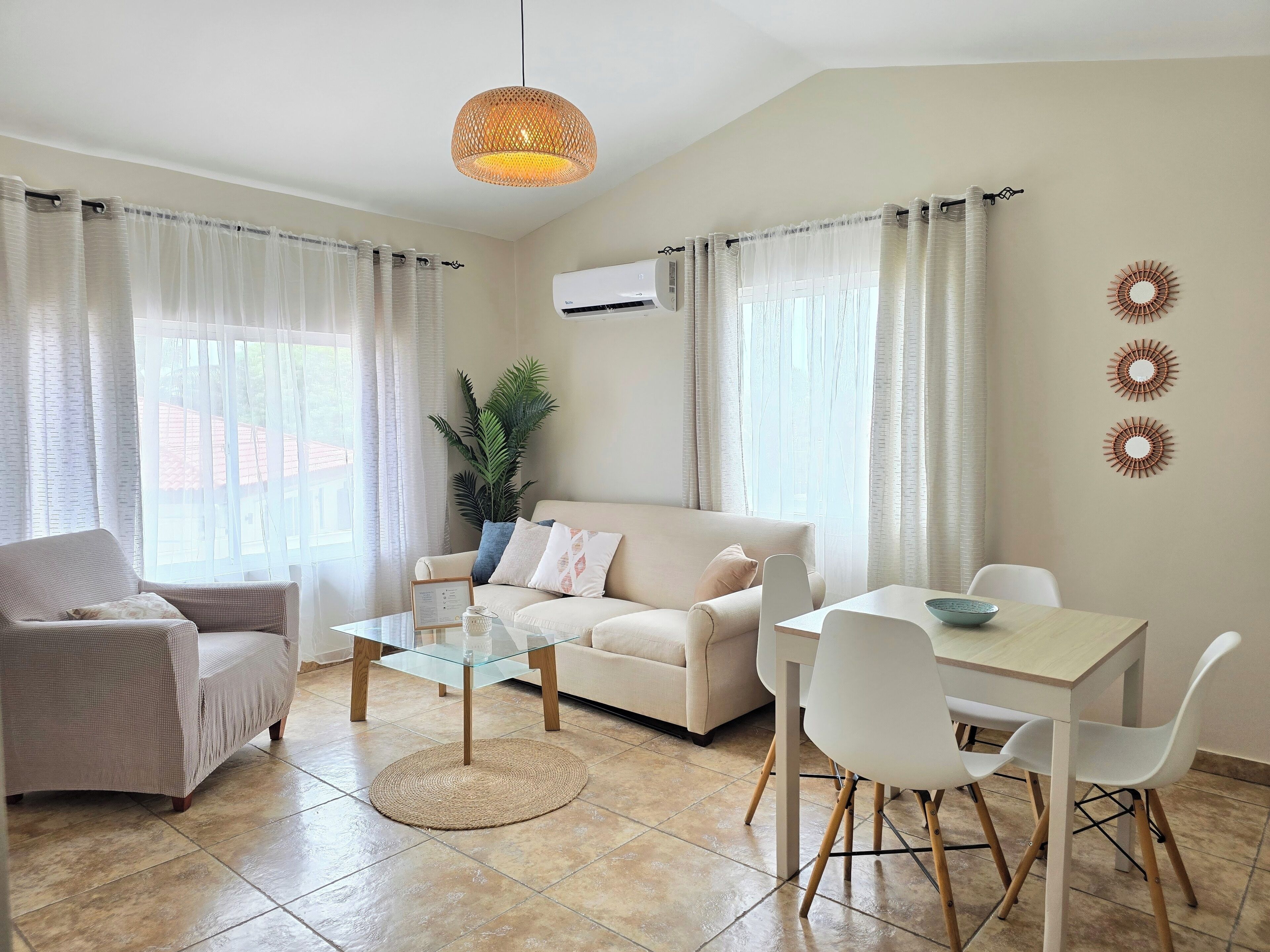 A modern living room with a sofa, a glass coffee table, a dining table with chairs, and a hanging light fixture.