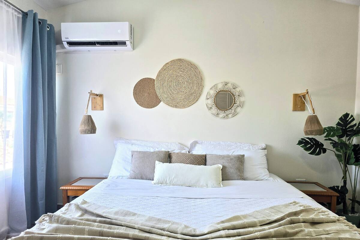 A neatly made bed with a striped blanket, a wall-mounted air conditioner, and two wall-mounted lamps.