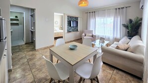 A modern, well-lit living room with a dining area, a sofa, and a TV mounted on the wall. - Rooi Santo Residence (Noord)