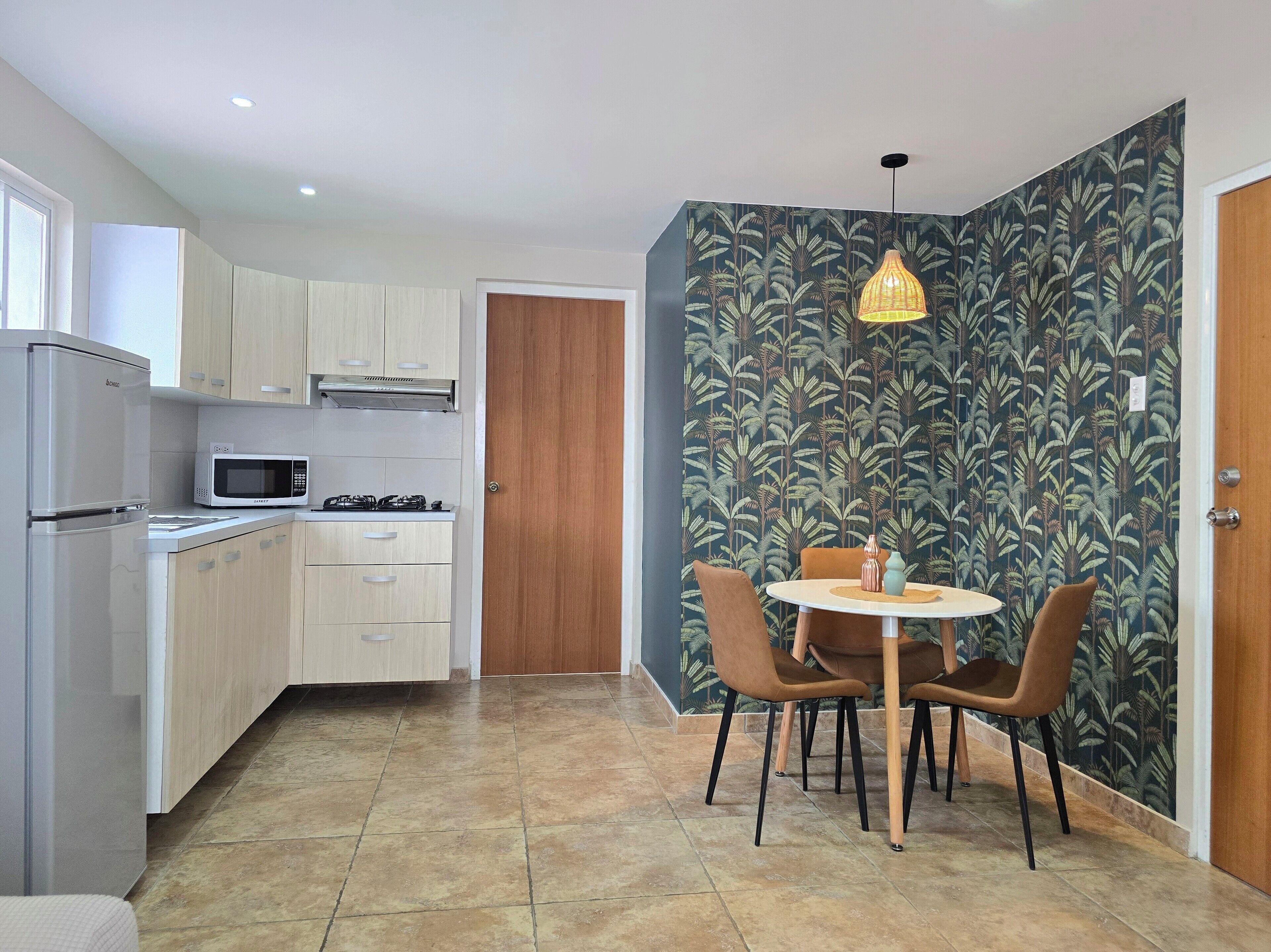 A compact kitchen with modern appliances, a dining area with a round table and chairs, and a door leading to another room.