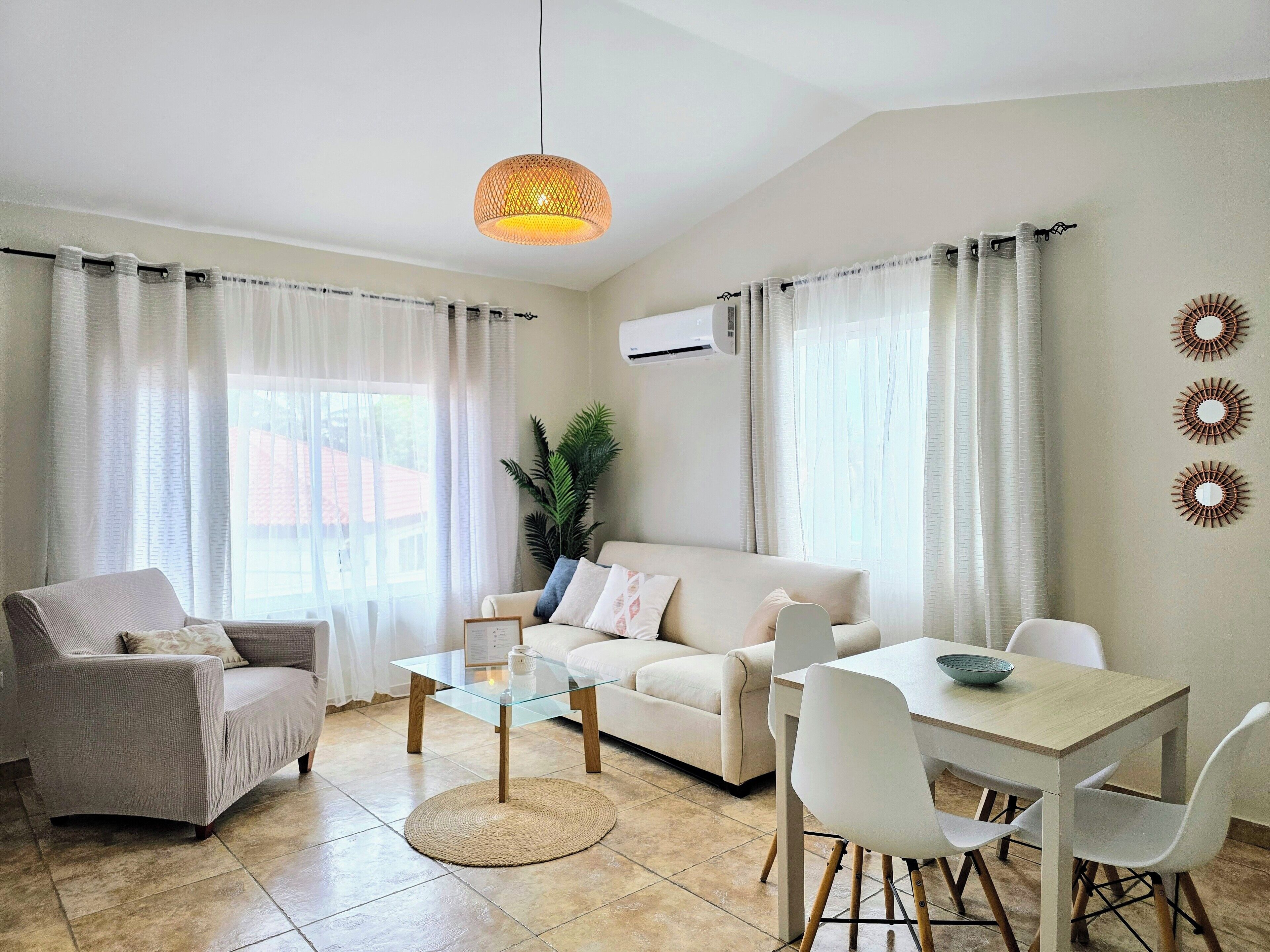 A modern living room with a glass coffee table, a sofa, a dining table with chairs, and a hanging light fixture.