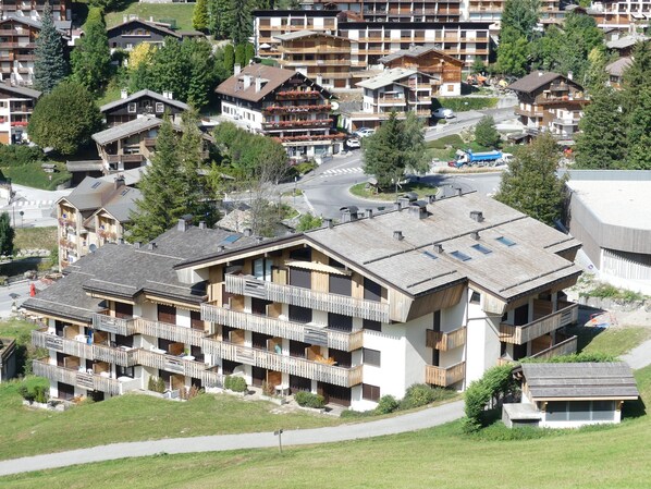 Een hotel met meerdere verdiepingen en balkons, een skilift op de achtergrond en een weg op de voorgrond.