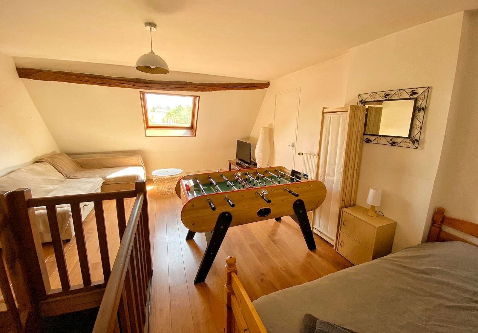 Una habitación acogedora con cama, mesa de futbolín, escritorio con lámpara y ventana que deja entrar luz natural.